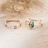 Shown here is "Artemis on the Vine", a branch-style moss agate women's engagement ring with diamonds, leaf accents and a floral tracer, laying together. Many other center stone options are available upon request.