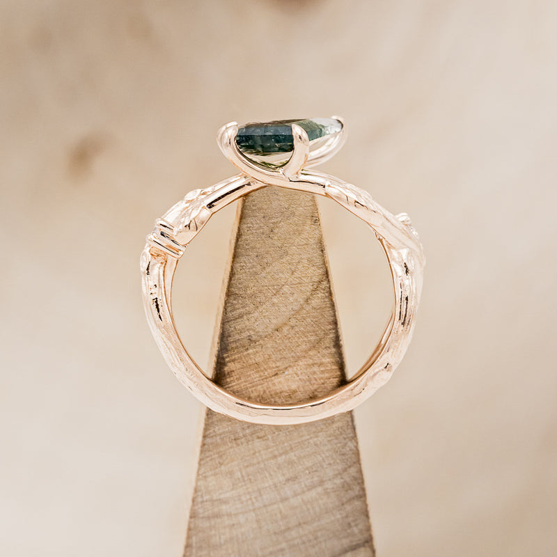 Shown here is "Artemis on the Vine", a branch-style moss agate women's engagement ring with diamond and leaf accents, side profile on stand. Many other center stone options are available upon request.
