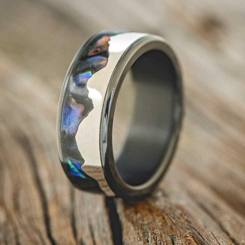 Shown here is "Helios", a custom, handcrafted men's wedding ring featuring a mountain range using pieces of silver and paua shell inlay, upright facing left. Additional inlay options are available upon request.