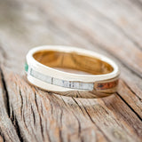 Shown here is "Four Corners", a custom, handcrafted men's wedding ring featuring 4 channels with antler, malachite, whiskey barrel oak and patina copper inlays on a 14K yellow gold lined band, tilted left. Additional inlay options are available upon request.