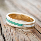 Shown here is "Four Corners", a custom, handcrafted men's wedding ring featuring 4 channels with antler, malachite, whiskey barrel oak and patina copper inlays on a 14K yellow gold lined band, tilted left. Additional inlay options are available upon request.