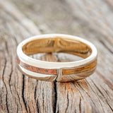 Shown here is "Four Corners", a custom, handcrafted men's wedding ring featuring 4 channels with antler, malachite, whiskey barrel oak and patina copper inlays on a 14K yellow gold lined band, laying flat. Additional inlay options are available upon request.