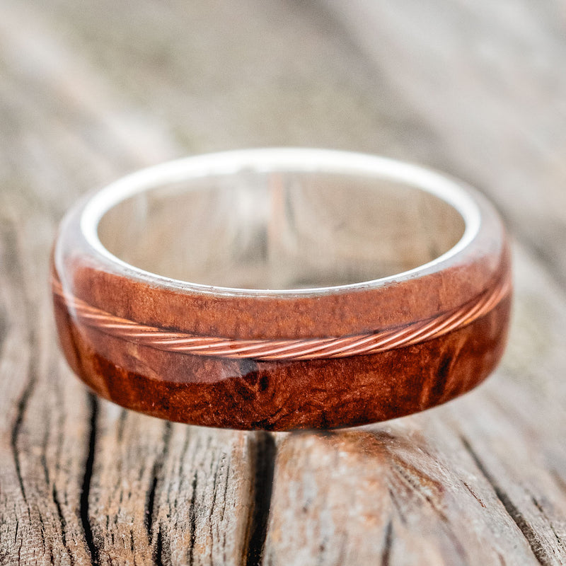 Shown here is "Remmy", a custom, handcrafted men's wedding ring featuring a redwood overlay and an offset twisted copper wire inlay, laying flat. Additional inlay options are available upon request.