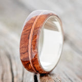 Shown here is "Remmy", a custom, handcrafted men's wedding ring featuring a redwood overlay and an offset twisted copper wire inlay, upright facing left. Additional inlay options are available upon request.