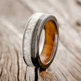 Shown here is "Raptor", a custom, handcrafted men's wedding ring featuring elk antler and iron ore inlays on a whiskey barrel oak lined black zirconium band, upright facing left. Additional inlay options are available upon request.