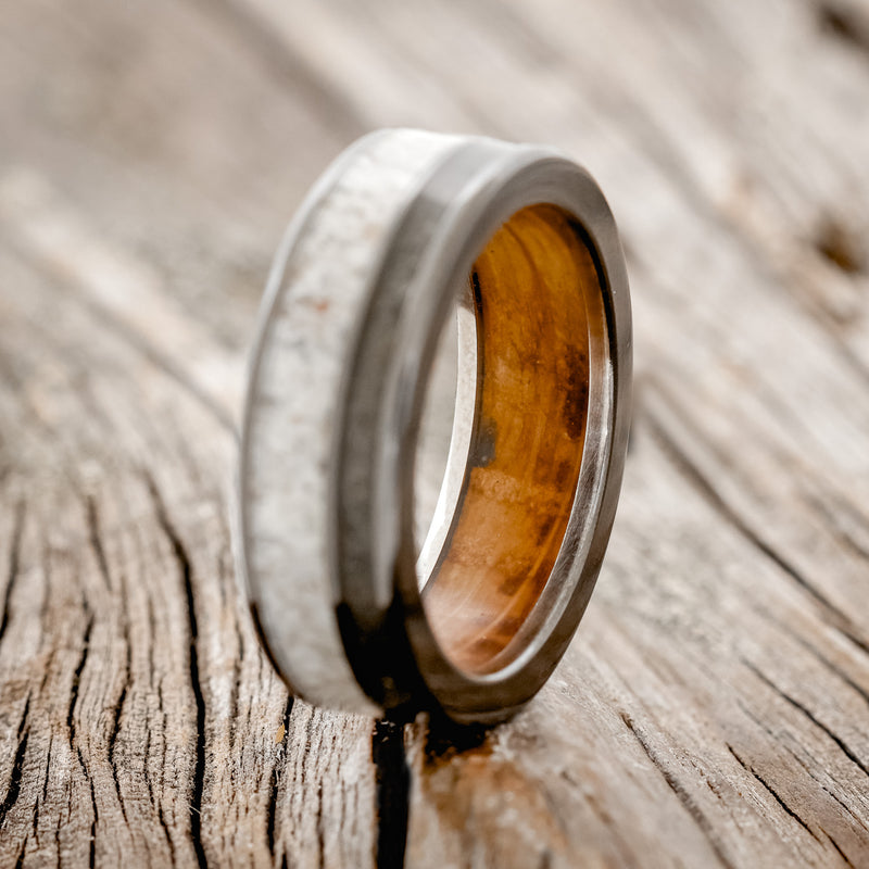 Shown here is "Raptor", a custom, handcrafted men's wedding ring featuring elk antler and iron ore inlays on a whiskey barrel oak lined black zirconium band, upright facing left. Additional inlay options are available upon request.