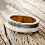 Shown here is "Raptor", a custom, handcrafted men's wedding ring featuring elk antler and iron ore inlays on a whiskey barrel oak lined black zirconium band, tilted left. Additional inlay options are available upon request.