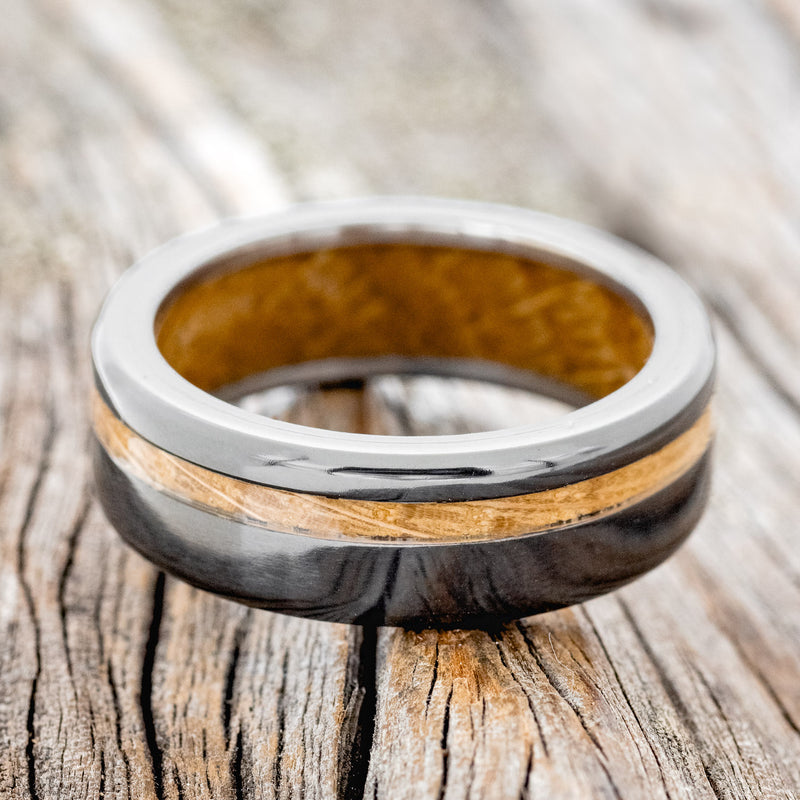 Shown here is "Vertigo", a handcrafted men's wedding ring featuring a whiskey barrel oak inlay and lining on a fire-treated black zirconium band, laying flat. Additional inlay and lining options are available upon request.