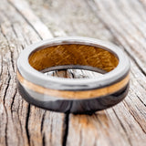 Shown here is "Vertigo", a handcrafted men's wedding ring featuring a whiskey barrel oak inlay and lining on a fire-treated black zirconium band, laying flat. Additional inlay and lining options are available upon request.