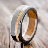 Shown here is "Vertigo", a handcrafted men's wedding ring featuring a whiskey barrel oak inlay and lining on a fire-treated black zirconium band, upright facing left. Additional inlay and lining options are available upon request.