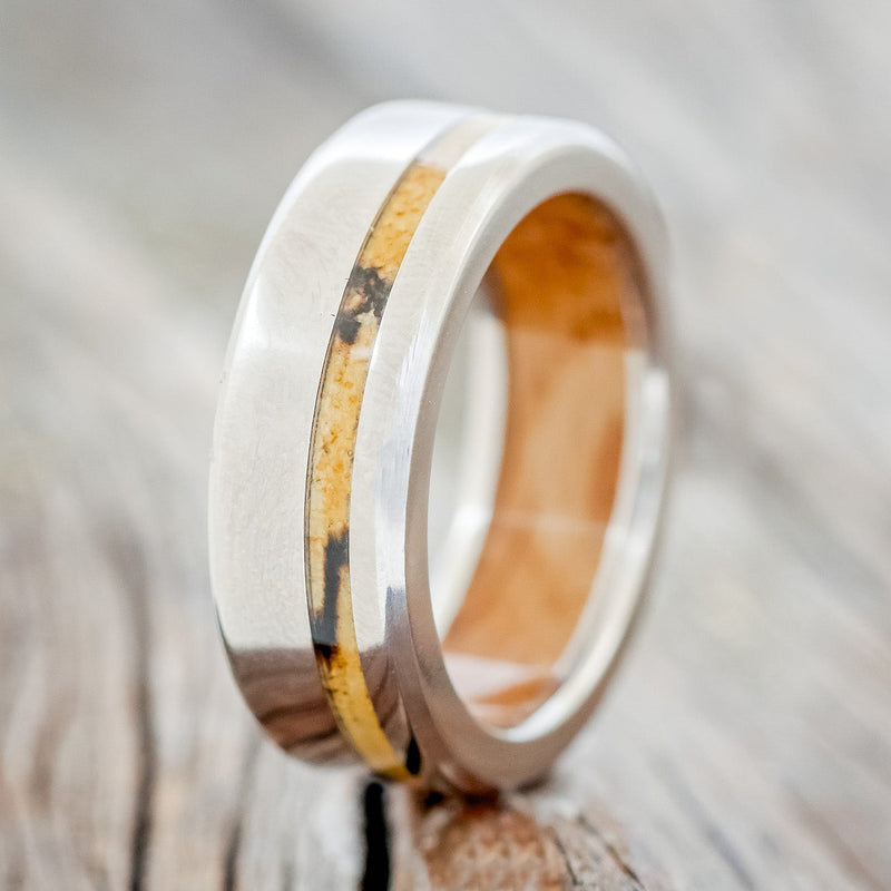 Shown here is "Vertigo", a handcrafted men's wedding ring featuring a spalted maple inlay on a whiskey barrel lined titanium band, upright facing left. Additional inlay options are available upon request.