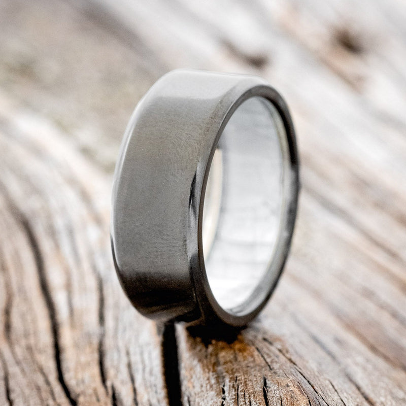 Shown here is a custom, handcrafted men's wedding ring featuring a mother of pearl lining shown here on a fire-treated black zirconium band, upright facing left. Additional inlay options are available upon request.