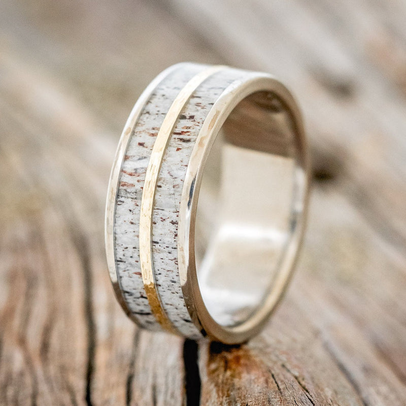Shown here is "Dyad", a custom, handcrafted men's wedding ring featuring 2 channels with antler inlays divided by a hammered 14K yellow gold inlay, shown here on a titanium band, upright facing left. Additional inlay options are available upon request.