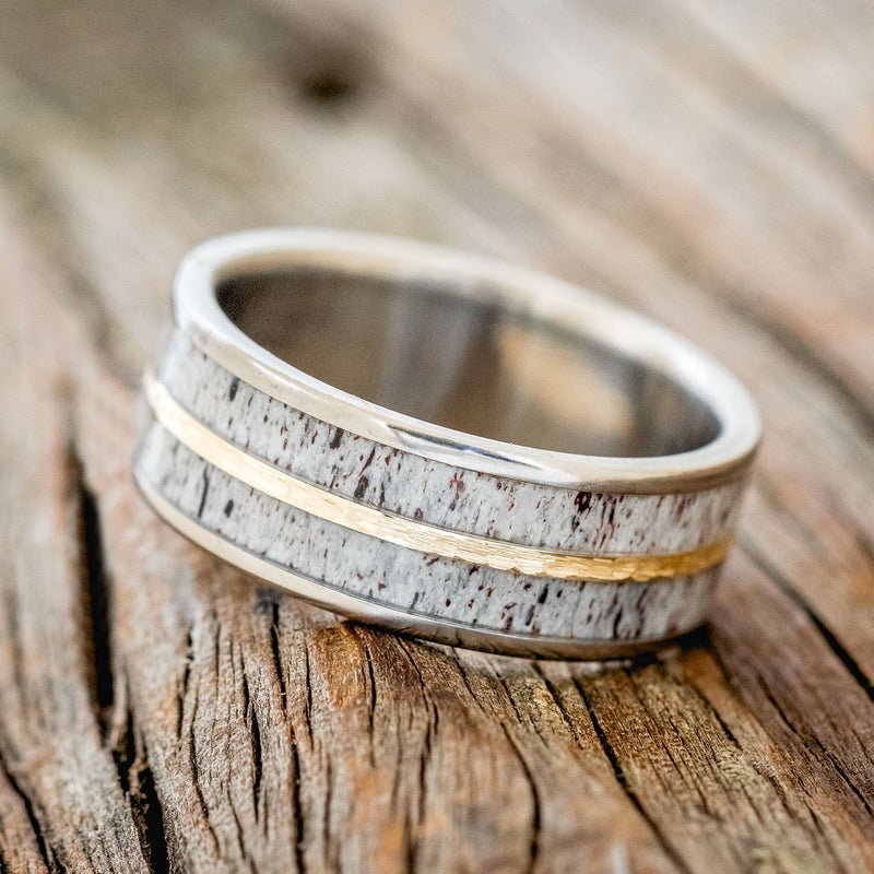 Shown here is "Dyad", a custom, handcrafted men's wedding ring featuring 2 channels with antler inlays divided by a hammered 14K yellow gold inlay, shown here on a titanium band, tilted left. Additional inlay options are available upon request.