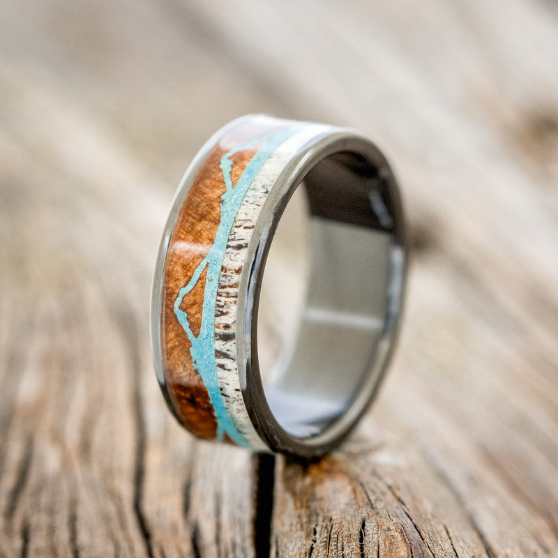 Shown here is "The Expedition", a custom, handcrafted men's wedding ring featuring a mountain engraving with redwood, antler and turquoise inlays, upright facing left. Additional inlay options are available upon request.