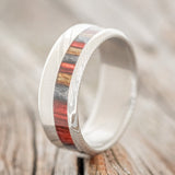 Shown here is "Castor", a custom, handcrafted men's wedding ring featuring a red, grey, and brown dyed birch wood inlay on a Damascus steel band, upright facing left. Additional inlay options are available upon request.