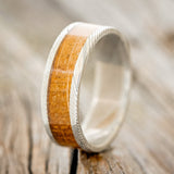 Shown here is "Kalder", a custom, handcrafted men's wedding ring featuring a whiskey barrel oak inlay on a Damascus steel band, upright facing left. Additional inlay options are available upon request.