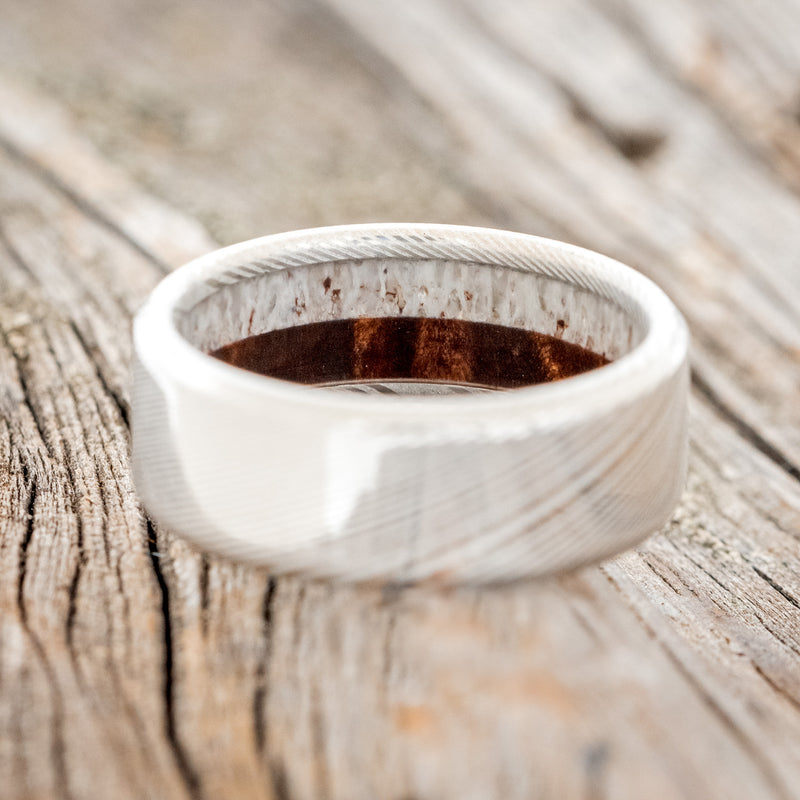 Shown here is a custom, handcrafted men's wedding ring featuring an elk antler and redwood lining, laying flat. Additional lining options are available upon request.