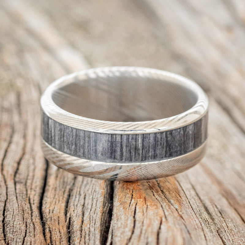Shown here is "Tanner", a custom, handcrafted men's wedding ring featuring a grey birch wood inlay, laying flat. Additional inlay options are available upon request.