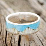 Shown here is "Helios", a handcrafted men's wedding ring featuring a mountain range using antler and a turquoise inlay, laying flat. Additional inlay options are available upon request.