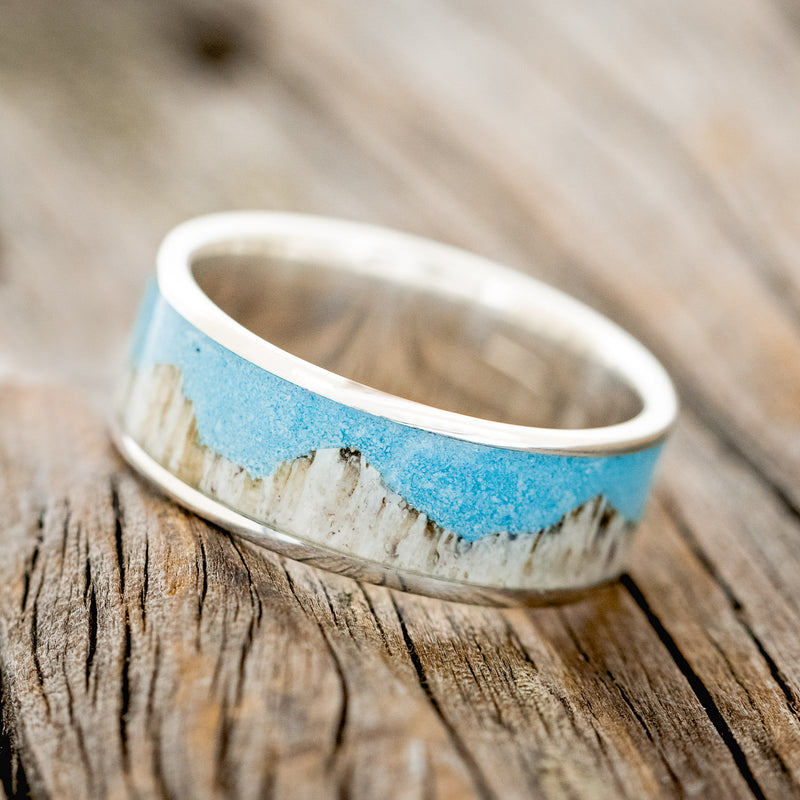 Shown here is "Helios", a handcrafted men's wedding ring featuring a mountain range using antler and a turquoise inlay, tilted left. Additional inlay options are available upon request.