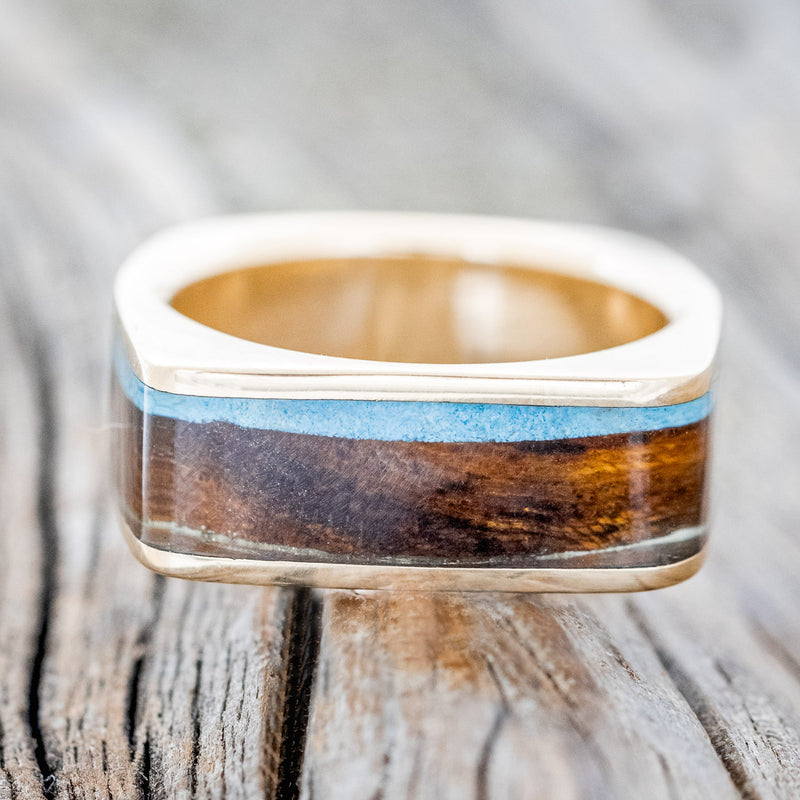 Shown here is "Mesa", a custom, handcrafted men's wedding band featuring a flat top 14K gold band with ironwood and turquoise inlays, laying flat. Additional inlay options are available upon request.