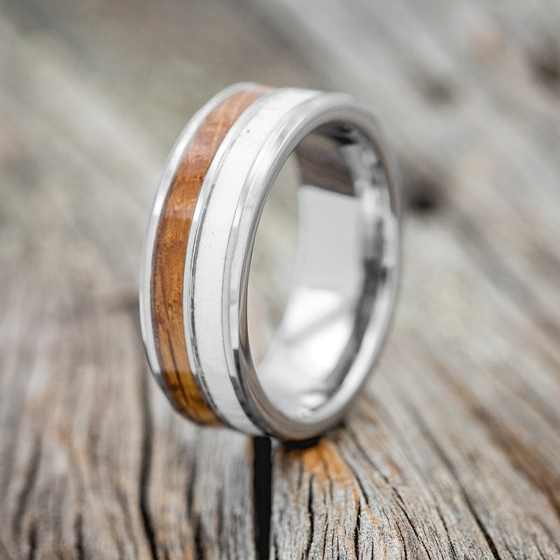 Shown here is "Dyad", a custom, handcrafted men's wedding ring featuring 2 channels with whiskey barrel wood and antler inlays, upright facing left.