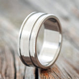 Shown here is "Ryder", a handcrafted men's wedding ring featuring a solid metal band that has two etched grooves and a brushed finish, upright facing left. 