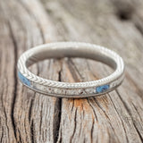 Shown here is "Eterna", a custom, handcrafted women's stacking band featuring antler and turquoise inlays on an etched Damascus steel band, laying flat. Additional inlay options are available upon request.