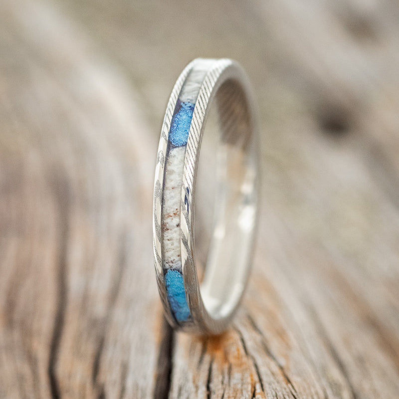 Shown here is "Eterna", a custom, handcrafted women's stacking band featuring antler and turquoise inlays on an etched Damascus steel band, upright facing left. Additional inlay options are available upon request.