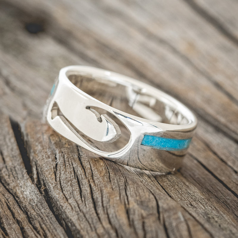 Shown here is "Hooked On You", a custom, handcrafted men's wedding ring featuring a fish hook shaped cut out and a turquoise inlay, tilted left. Additional inlay options are available upon request.