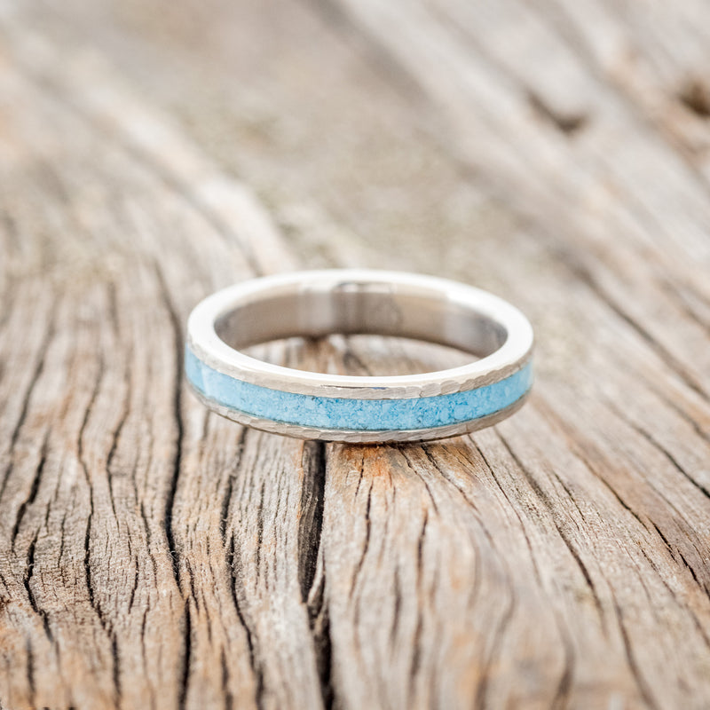 Shown here is "Perenna", a custom, handcrafted women's stacking band featuring a turquoise inlay on a titanium band with a hammered finish, laying flat. Additional inlay options are available upon request.
