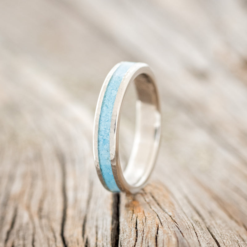 Shown here is "Perenna", a custom, handcrafted women's stacking band featuring a turquoise inlay on a titanium band with a hammered finish, upright facing left. Additional inlay options are available upon request.