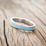 Shown here is "Perenna", a custom, handcrafted women's stacking band featuring a turquoise inlay on a titanium band with a hammered finish, tilted left. Additional inlay options are available upon request.