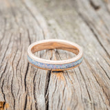 Shown here is "Perenna", a custom, handcrafted women's stacking band featuring a fire and ice opal inlay on a 14K gold band, laying flat. Additional inlay options are available upon request.
