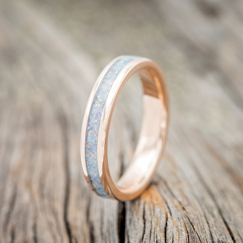 Shown here is "Perenna", a custom, handcrafted women's stacking band featuring a fire and ice opal inlay on a 14K gold band, upright facing left. Additional inlay options are available upon request.