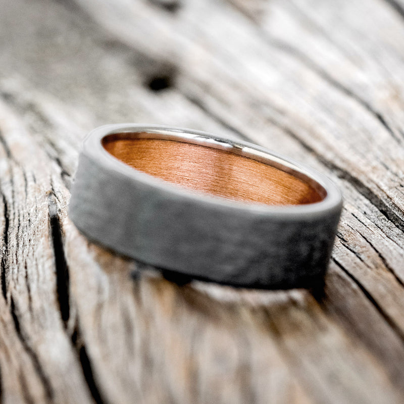 Shown here is a handcrafted men's wedding ring featuring a rustic copper lining with a hammered black zirconium band, tilted left Additional lining options are available upon request.