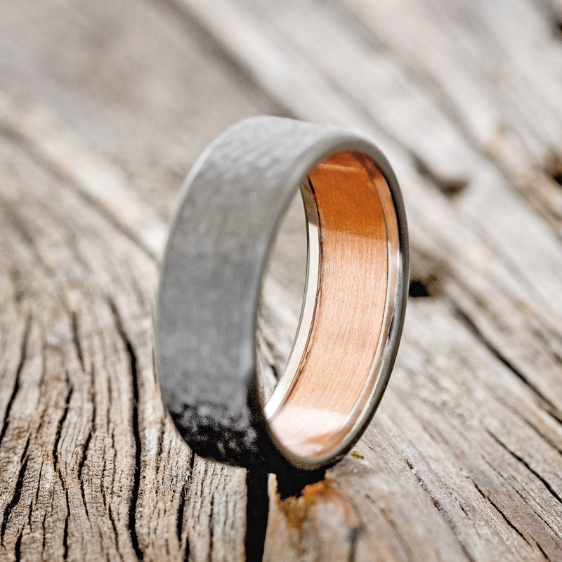 Shown here is a handcrafted men's wedding ring featuring a rustic copper lining with a hammered black zirconium band, upright facing left Additional lining options are available upon request.