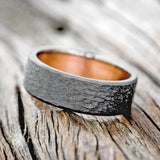 Shown here is a handcrafted men's wedding ring featuring a rustic copper lining with a hammered black zirconium band, tilted left Additional lining options are available upon request.