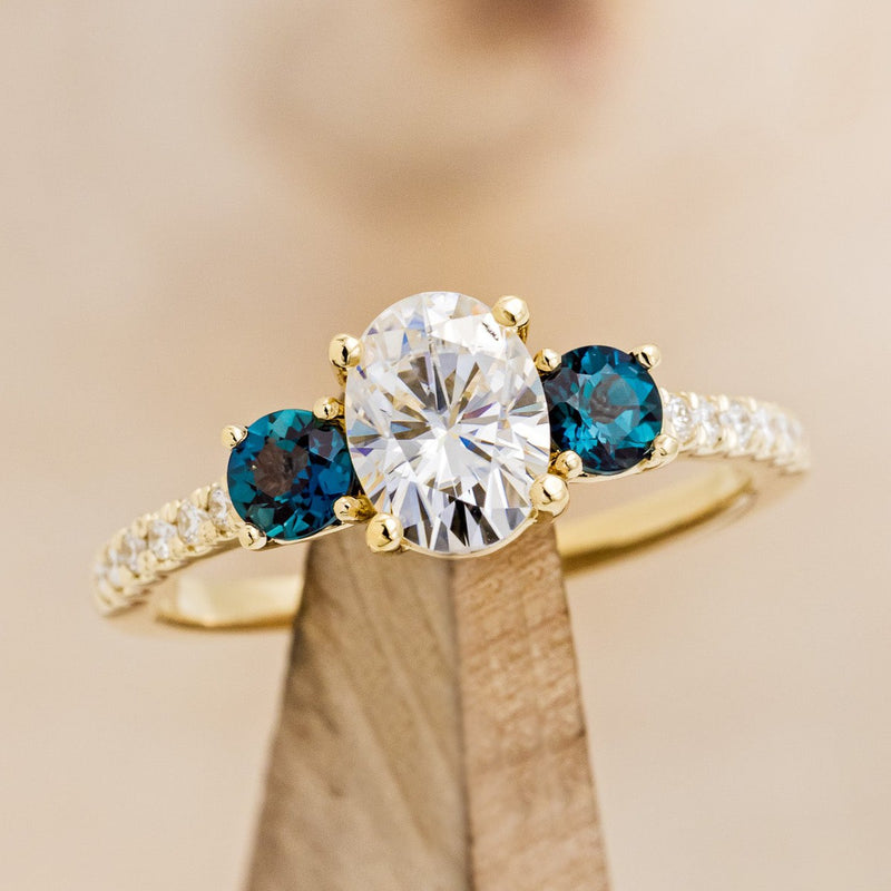 Shown here is "Cosette", a moissanite and lab-created alexandrite women's engagement ring with diamond accents, on stand front facing. many center stone options are available upon request.
