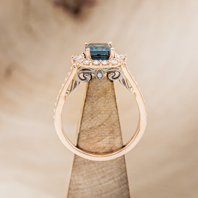 Shown here is "Ophelia", a lab-created alexandrite women's engagement ring with a diamond halo and diamond accents, side view on stand. Many other center stone options are available upon request.