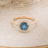 Shown here is "Coralie", a women's engagement ring with a lab-created alexandrite center stone with a starburst diamond halo, front facing. Many other center stone options are available upon request.