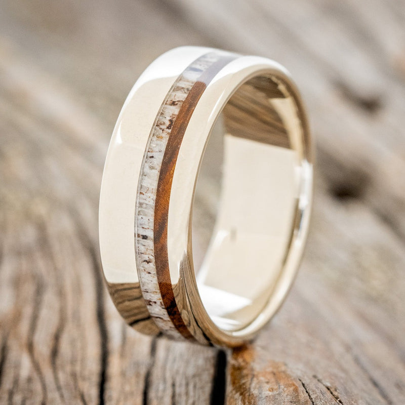 Shown here is "Castor", a custom, handcrafted men's wedding ring featuring ai ironwood and antler inlay on a 14K gold band, upright facing left. Additional inlay options are available upon request.
