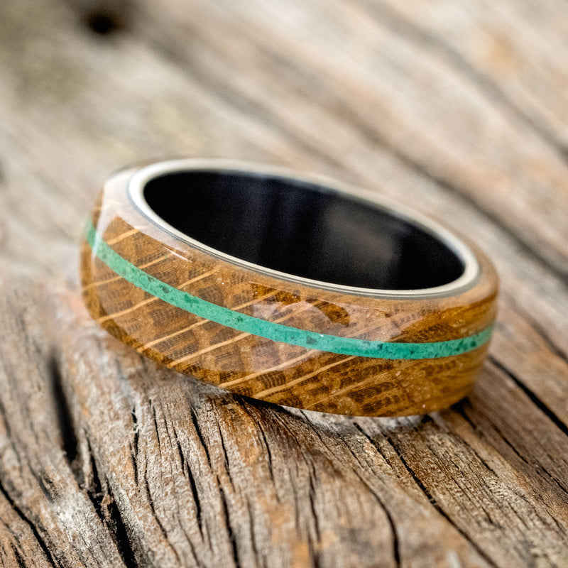 Shown here is "Remmy", a custom, handcrafted men's wedding ring featuring a whiskey barrel oak overlay and an offset malachite inlay on a fire-treated black zirconium band, tilted left. Additional inlay options are available upon request.