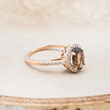 Shown here is "Diana", an oval smoky quartz women's engagement ring with a diamond halo and diamond accents, facing right. Many other center stone options are available upon request.
