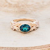 Shown here is "Elora", a vintage-style oval lab-created alexandrite women's engagement ring with floral details and moonstone accents, front facing. Many other center stone options are available upon request.