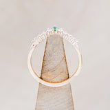 Shown here is "Sage" tracer, an emerald women's band with diamond accents, side view on stand. Many other center stone options are available upon request.