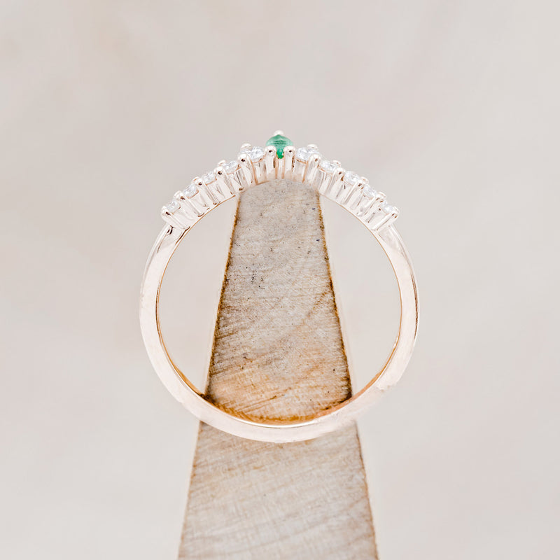 Shown here is "Sage" tracer, an emerald women's band with diamond accents, side view on stand. Many other center stone options are available upon request.