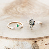Shown here is "Sage", a moss agate women's engagement ring with diamond accents and an emerald tracer, laying together. Many other center stone options are available upon request.