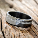 Shown here is "Vertigo", a custom, handcrafted men's wedding ring featuring an offset moonstone inlay on a fire-treated black zirconium band, tilted left. Additional inlay options are available upon request.